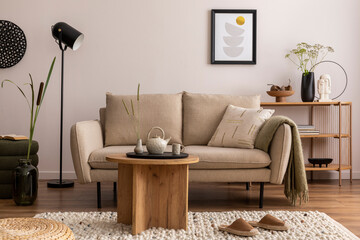 Domestic and cozy interior of living room with beige sofa, wooden shelf, pouf, furniture, green...