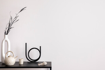 Aesthetic interior of living room with copy space, white wall, black table, candlestick, vase with dried flowers, pitcher, and elegant personal accessories. Stylish home decor. Template.