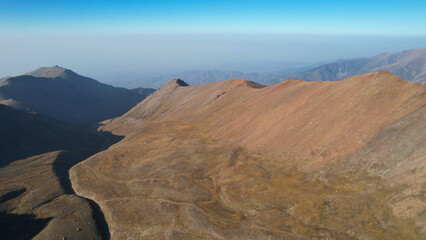 Autumn mountains. The river dried up in the gorge. Top view from the drone on yellow grass and sometimes green bushes. The riverbed is almost dry. Gray smog can be seen in the distance. Kazakhstan