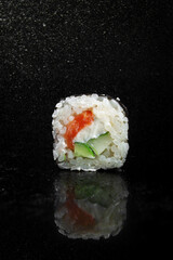 Sushi rolls with rice, salmon and cucumber on black background with reflection and splashes of water