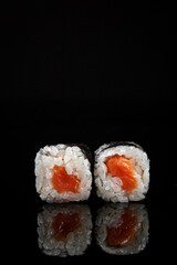 Sushi rolls with rice and salmon on a black background with reflection
