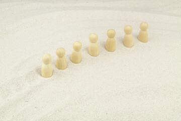 Fototapeta na wymiar Several wooden people figures in row on sand background. Travel in dessert and caravan concept.