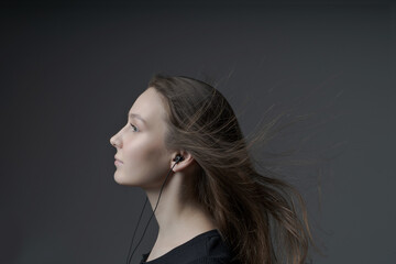Fototapeta premium The girl listens to music in headphones on a dark background with developing hair