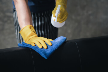 Person cleaning the room, cleaning staff is using cloth and spraying disinfectant to wipe the sofas in the company office room. Cleaning staff. Maintaining cleanliness in the organization.