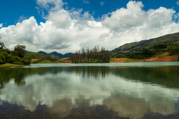 Towering mountains, river with visible small island, blue and white sky, reflection visible in water, nature's gift of greenery everywhere is the way one can explain the beauty of Ooty.