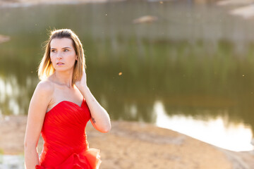 Beautiful young woman with clean perfect skin wearing a classy red evening dress. Portrait of beauty model with natural nude makeup. Spa, skin care and wellness. Close up,natural background, copyspace