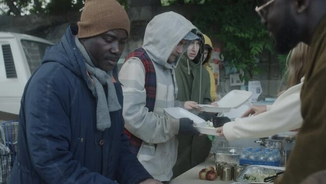 Group of homeless people getting free food from volunteers on outdoor soup kitchen
