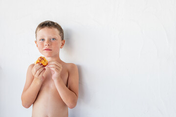 Adorable shirtless little kid eating yummy fruit against white wall