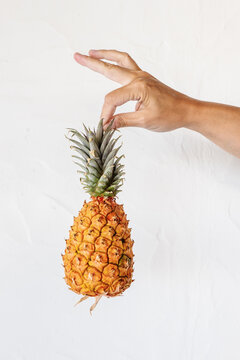 Crop faceless person showing ripe pineapple against white background