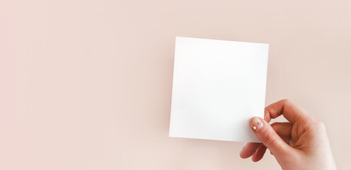 Banner of female hand with festive minimalistic natural manicure holding white piece of paper for notes with space for text. Concept of creativity, holiday wish, plans for future, art. Copy space