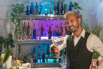 Elegant barman smiling on bar counter with a cocktail in his hand. Toasting in the air.