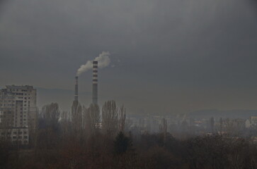View of a gloomy winter day with fallen leaves from deciduous trees in a residential area against the background of the working chimneys of the Sofia Thermal Power Plant, Bulgaria 