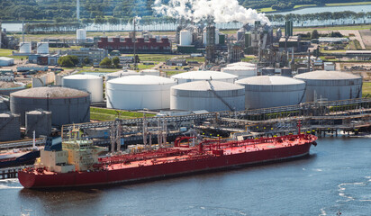 Oil tanker moored an oil terminal with fuel storage silos in an industrial port