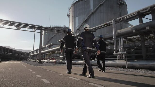 Group oil workers walking in front fuel tanks