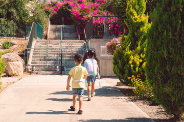 Fototapeta premium A young children going back to school. Little girl with a tie dye backpack walks to preschool with her brother at a sunny day.