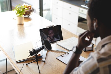 Happy african american man sitting at table in kitchen using tablet for video call