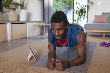 Happy african american man exercising, using tablet in living room