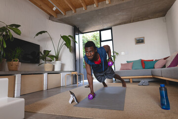 Happy african american man exercising, using tablet in living room