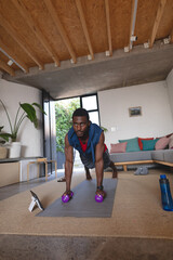 Happy african american man exercising, using tablet in living room