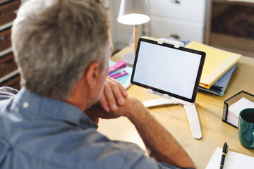 Caucasian man sitting at table in kitchen and using tablet with copyspace