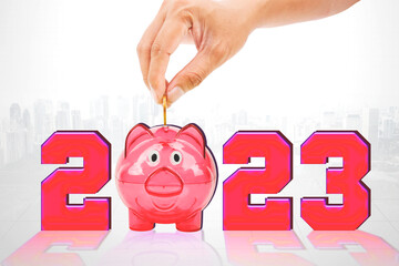Hand putting coins in piggy bank with numbers 2023