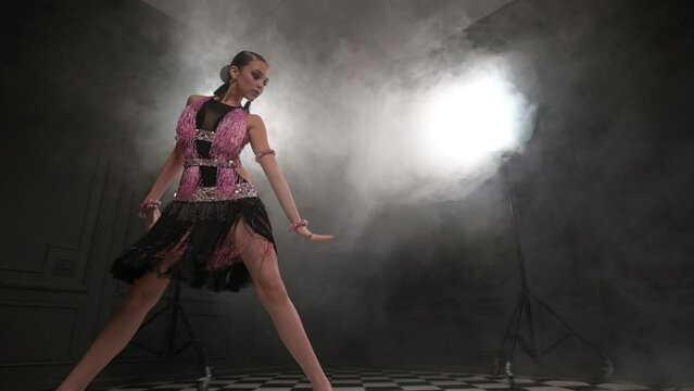 attractive teenage girl dancing solo ballroom sport dancing latino in a dark studio room filled with smoke. Professional dance sport