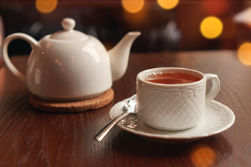 White cup with teapot. Pot standing on saucer in soft focus on naturally blurred background. Coffee, tea house, bokeh lights. The concept of a cozy pastime, tea ceremony