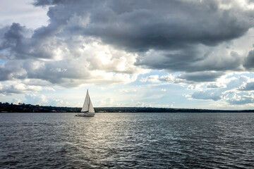 Small sailing boat sailing alone lit by the sun in overcast day
