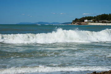 A sea pebble beach with an incoming foam wave. In the distance, on the horizon, mountains.