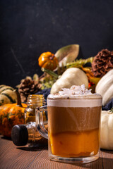 Glass cup with tasty pumpkin spice latte, with white and orange pumpkin squash, pumpkin pie spices and autumn decor copy space. Traditiional autumn Thanksgiving holiday drink