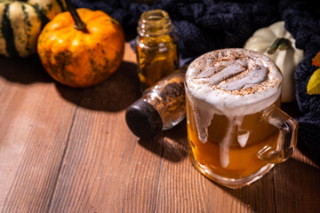 Glass cup with tasty pumpkin spice latte, with white and orange pumpkin squash, pumpkin pie spices and autumn decor copy space. Traditiional autumn Thanksgiving holiday drink
