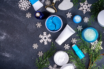 Fototapeta na wymiar Winter skin care and hand care cosmetic in unbranded containers, bottles, tubes with artificial snowflakes on black stone background. Winter hand skin care cosmetics background top view copy space