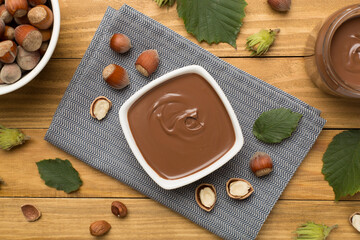 Hazelnut cream with nuts and green leaves on wooden background, top view