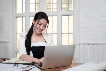 Charming smiling motivated woman architect working on building plan using laptop computer. Engineer designing virtual sketch for futuristic construction.