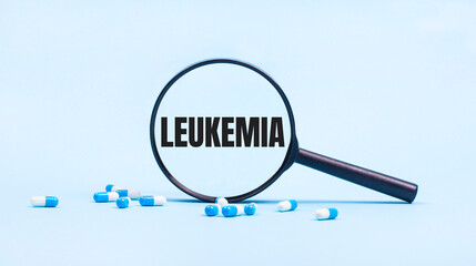 On a blue background, white and blue capsules with pills and a black magnifying glass with the text LEUKEMIA. Medical concept.