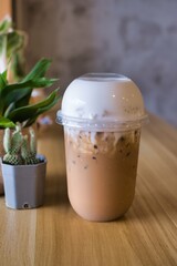delicious iced milk foamy cappuccino in plastic take away cup at front wooden counter bar with small cactus and plants