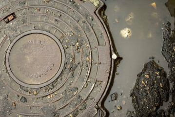 Sewer manhole in the water on the road. Manhole on a destroyed asphalt road