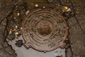 Sewer manhole in the water on the road. Manhole on a destroyed asphalt road