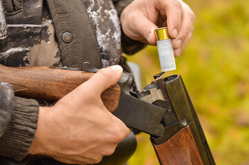 Selective focus of the hands of a man in a camouflage protective suit who loads a double-barreled shotgun. The concept of hunting.