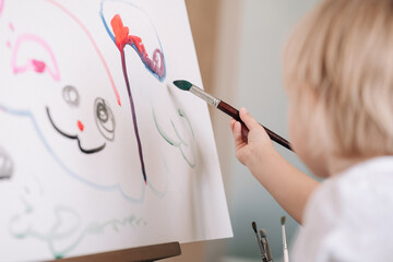 Child is painting with paintbrush. Child drawing on the easel. The hand and paint brush. Closeup, selective focus