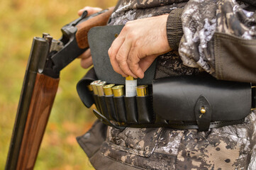 Close-up of a hunter, holding a gun in his hands, a leather bandolier with cartridges on his belt. Process of hunting during season. Selective focus.