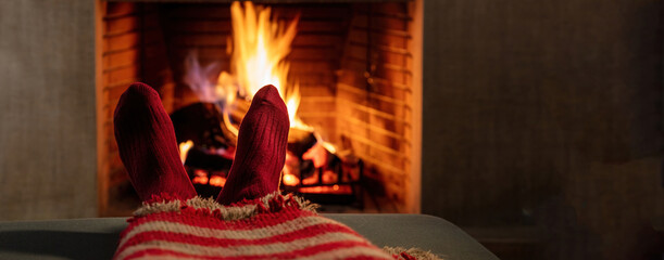 Man relaxing at the burning fireplace. Warm socks and blanket, fireside and flames background.