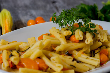 Pasta with courgettes, courgette flowers, yellow datterini tomatoes served in a white plate. Vegetarian recipe