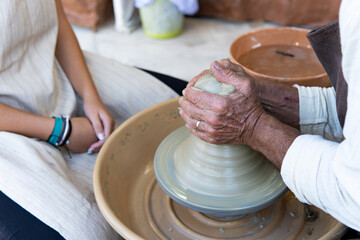 Potters working to shape the clay on the spinning wheel in the workshop. Tanned hands