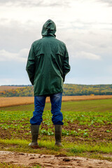 A man in a field after a thunderstorm looks into the distance. The guy in the raincoat looks at the...