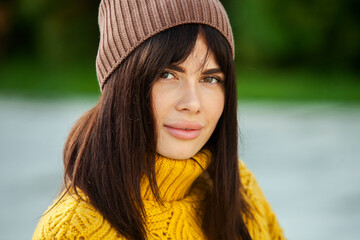 Beautiful European brunette dressed in a yellow woolen sweater and hat outside. The beautiful girl who wears thick stylish autumn clothes in cool weather.