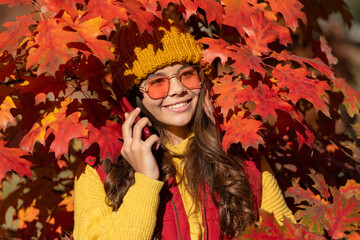 Child girl in autumn fall park outdoor, kids fun face. happy teen kid in sunglasses talking on phone at autumn leaves on natural background