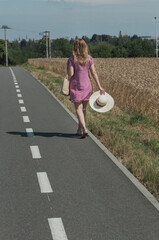 A girl walking along a wheat field with a straw hat.