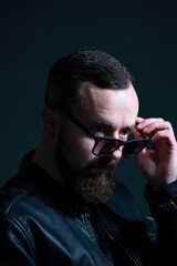 dramatic portrait of bearded millennial guy in leather jacket on dark background