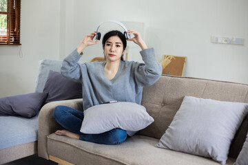 Happy Asian young woman wearing headphones sitting relaxing on sofa at home.
